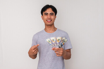 Happy young Asian man standing and holding cash with a cheerful expression, isolated on white...
