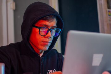 Masked hacker typing on laptop in dark room, surrounded by code screen. Cyber ​​security,...