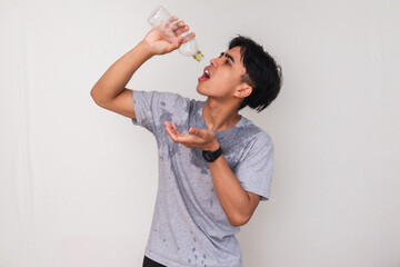 Tired young Asian man sweating and holding an empty water bottle with a disappointed expression,...