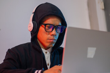 Masked hacker typing on laptop in dark room, surrounded by code screen. Cyber ​​security,...
