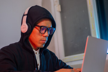 Masked hacker typing on laptop in dark room, surrounded by code screen. Cyber ​​security,...