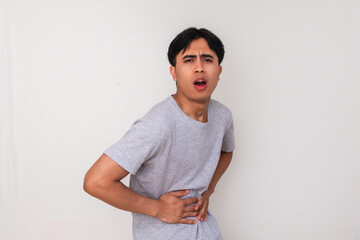 Funny young Asian man holding his stomach with a painful face as if having constipation. Isolated...