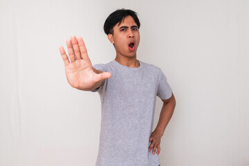 Portrait of a serious young Asian man making a stop hand gesture while looking at the camera,...