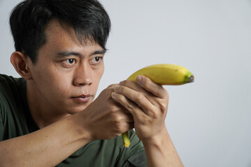 A man with a serious expression holds a yellow banana like a handgun, aiming forward, creating a...
