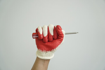 Hand wearing a red and white work glove firmly grips a screwdriver, ready for repair or...