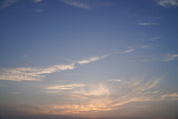 A tranquil natural background of a serene blue sky at dusk, with soft wispy cirrus clouds illuminated by the warm glow of the setting sun
