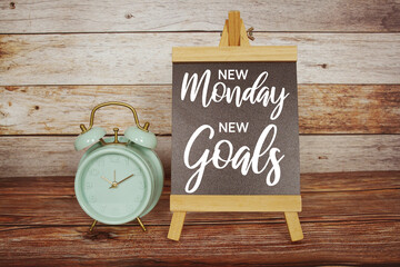 Inspiration quote "New Monday New Goals text message with green alarm clock on wooden background