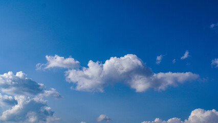 Peaceful skyscape featuring a vast, azure sky and gentle, puffy white clouds floating in the bright...