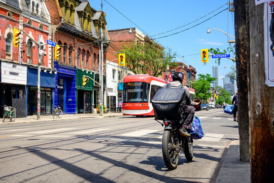 Gig economy: a food delivery person on an electric bike on a big city arterial street with tram and traffic lights in background in summer shot in Toronto&rsquo;s Queen West district