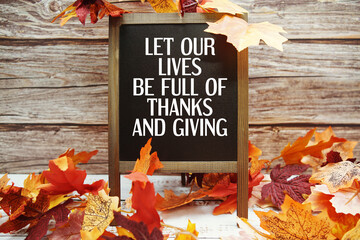 Let Our Lives Be Full Of Thanks And Giving text with maple leaf decoration on wooden background