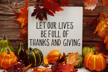 Let Our Lives Be Full Of Thanks And Giving text with maple leaf decoration on wooden background