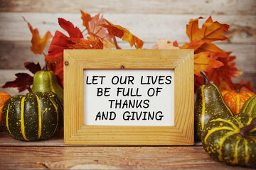 Let Our Lives Be Full Of Thanks And Giving text with maple leaf decoration on wooden background