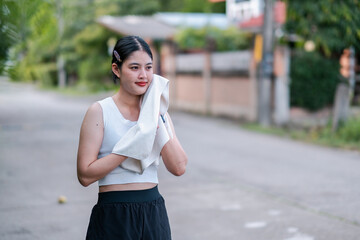 A young woman in athletic attire uses a towel to cool down after exercising outdoors in a suburban...