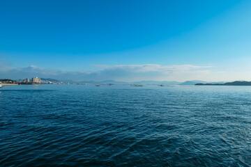 Calm blue sea stretches towards distant coastline and mountains near Miyajima, Japan. Serene seascape features traditional oyster farms, capturing tranquil beauty of the Seto Inland Sea on a clear day