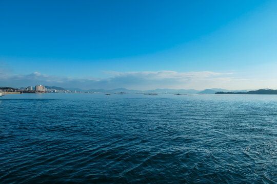 Calm blue sea stretches towards distant coastline and mountains near Miyajima, Japan. Serene seascape features traditional oyster farms, capturing tranquil beauty of the Seto Inland Sea on a clear day