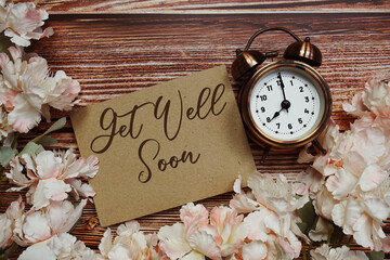Get Well Soon text with alarm clock and flowers decoration on wooden background