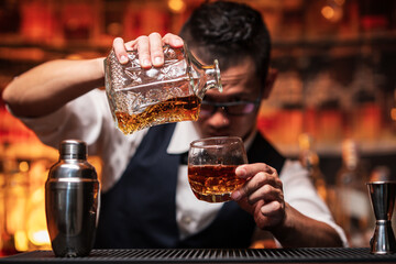 Bartender is pouring whiskey into a glass a customer's glass.	