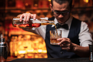 Bartender is pouring whiskey into a glass a customer's glass.