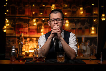 Handsome businessman or young man sits, drinks whiskey, looks stressed and sad.