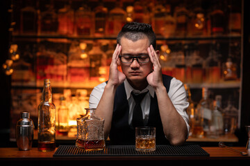 Handsome businessman or young man sits, drinks whiskey, looks stressed and sad.