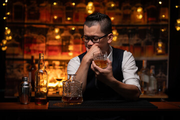Handsome businessman or young man sits, drinks whiskey, looks stressed and sad.
