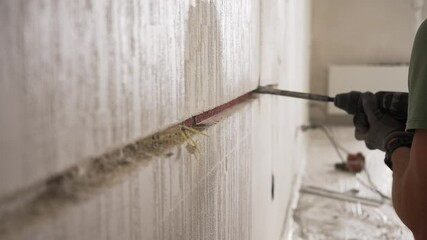 Professional construction worker using a rotary hammer drill to gouge a concrete wall, creating a channel for cable laying during a house renovation