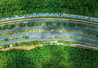 Top-down view of a clean multi-lane highway cutting through a dense and vibrant green forest.