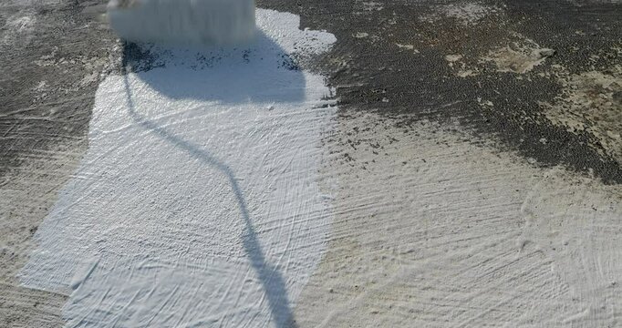 POV. Painter applying a fresh white waterproof coat paint with a roller tool to a roof surface.