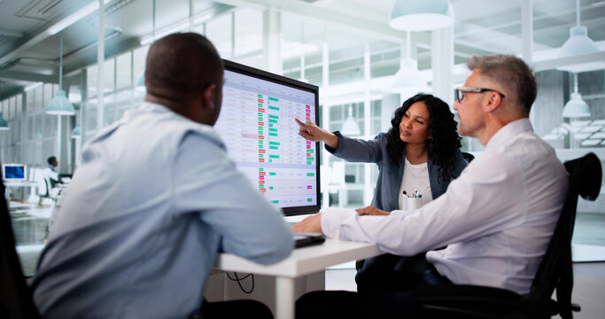 Business Team Analyzing Reports On Multiple Computer Screens In Workplace
