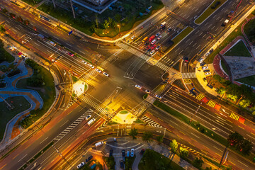 Aerial view of a busy urban road intersection with traffic and glowing street lights at night.