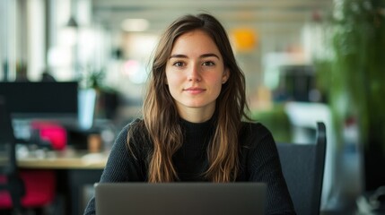 A young female software developer is focused on her laptop in a modern office setting. Her serious expression reflects determination and creativity in her work.