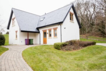 White cottage is standing on brick walkway in flat design with slate roof and colored bins