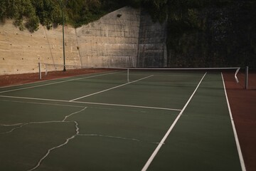 Flat design tennis court surface is showing cracks, white lines and sagging net with lamp post