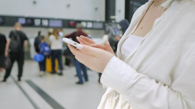 Woman is holding a cell phone in a busy airport. The scene is bustling with people and luggage, creating a sense of urgency and movement