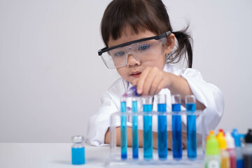 A young child in protective eyewear conducts an experiment with colorful liquids in test tubes,...