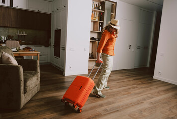 cheerful woman wearing a hat pulls her bright orange suitcase through a stylish indoor space, ready...