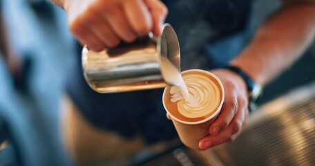 Barista is pouring milk into a takeaway coffee cup, creating latte art with steamed milk in a coffee shop