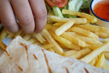 Child hand reaches for crispy fries beside a fresh salad and salsa