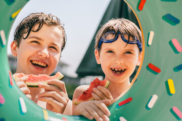 Happy kids smiling and eating watermelon through colorful pool float on a bright sunny day