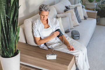 Senior woman checks blood pressure at home with digital monitor, daily health care routine