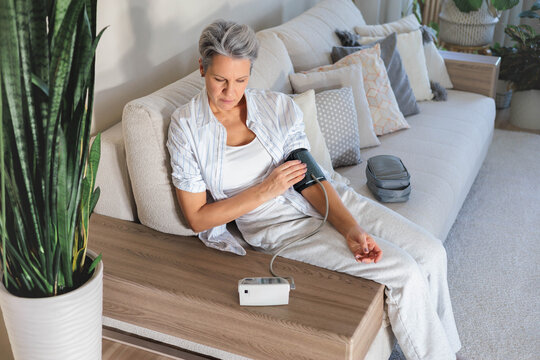 Senior woman checks blood pressure at home with digital monitor, daily health care routine