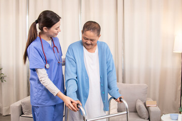 Young nurse assisting senior woman in walking with a walker, demonstrating caregiving,...