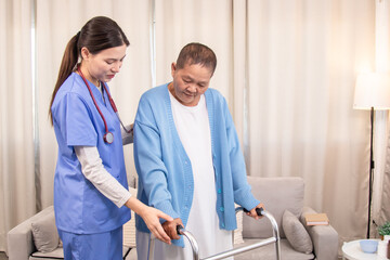 Young nurse assisting senior woman in walking with a walker, demonstrating caregiving,...