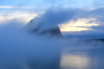 Fototapeta premium Misty mountain peak at sunrise over calm water