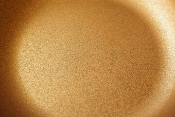 Close-up of a golden non-stick frying pan surface with a textured coating, showing the heat distribution pattern and metallic sheen.