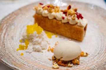 A tart with cream on top, with vanilla ice cream and crumble served on plate.