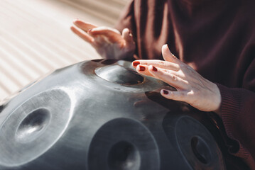 young caucasian woman playing black handpan with hands, ethnic metal drum instrument, sits on...