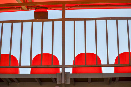 A metal railing with red chairs on it. The chairs are red and ar