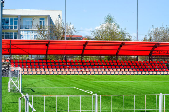 A soccer field with a red roof and a fence. The field is empty.