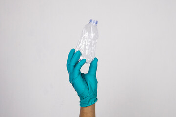 Hand wearing work gloves is holding an empty plastic bottle isolated on white background